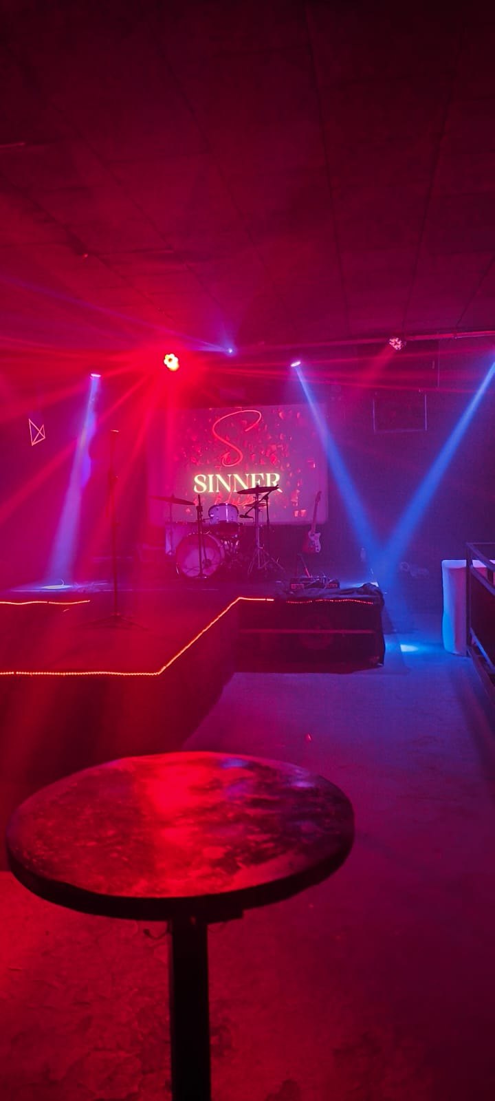 Palco montado com bateria e iluminação cênica em vermelho e azul.